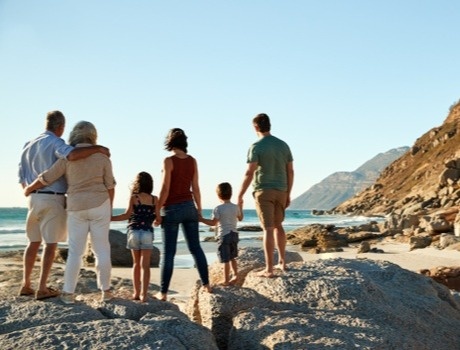 Family standing on the shore, gazing out at the beach and ocean waves in the distance